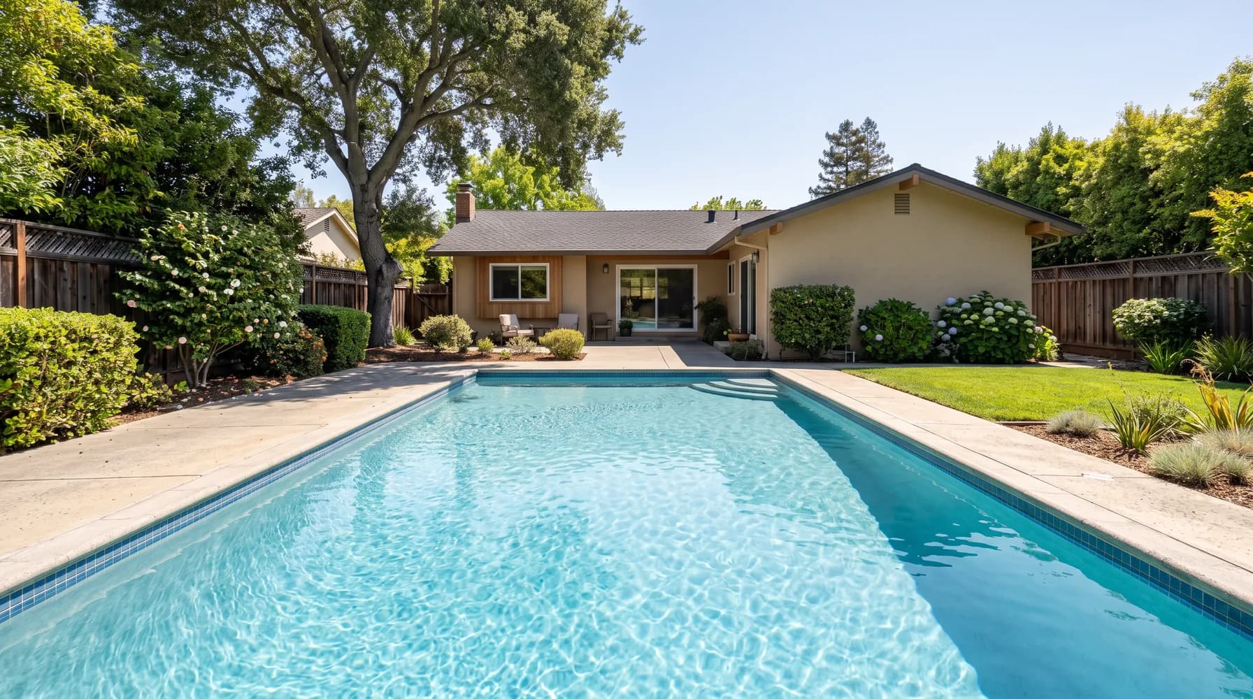 Rectangular backyard pool with clear blue water behind a single-story East Bay home