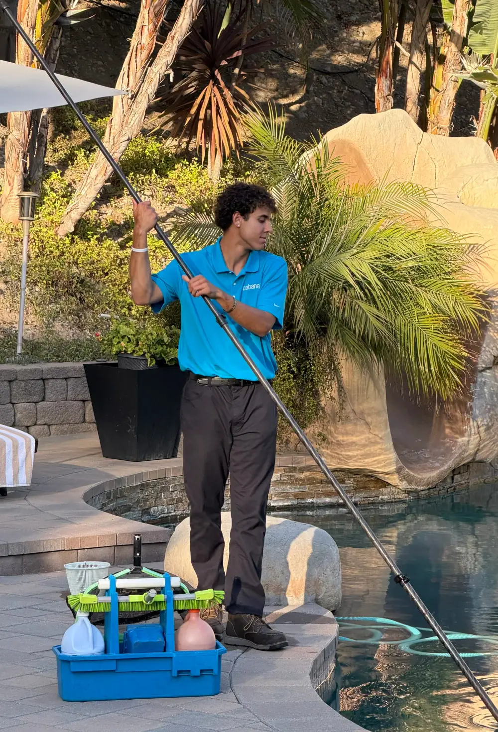 Cabana pool technician in branded polo vacuuming a backyard pool