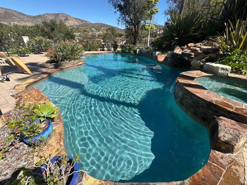 Sparkling blue pool with curved steps, a raised stone spa, rock waterfall feature, and lush landscaping, after pool service in 4S Ranch, CA