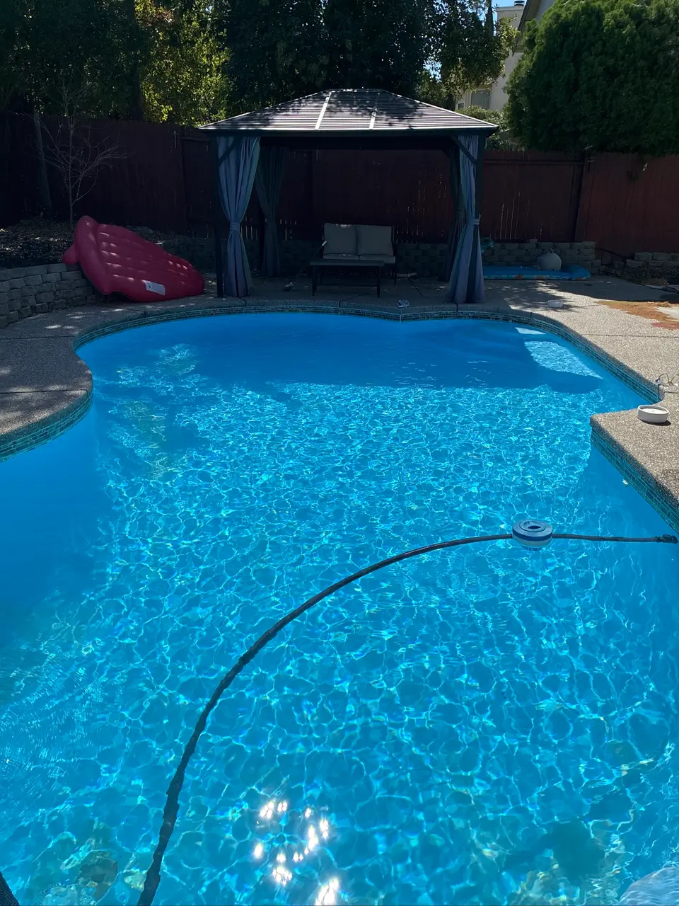 Sparkling blue water fills a freeform pool with submerged steps, waterline tile, and a gazebo behind it, after pool service in Antelope, CA