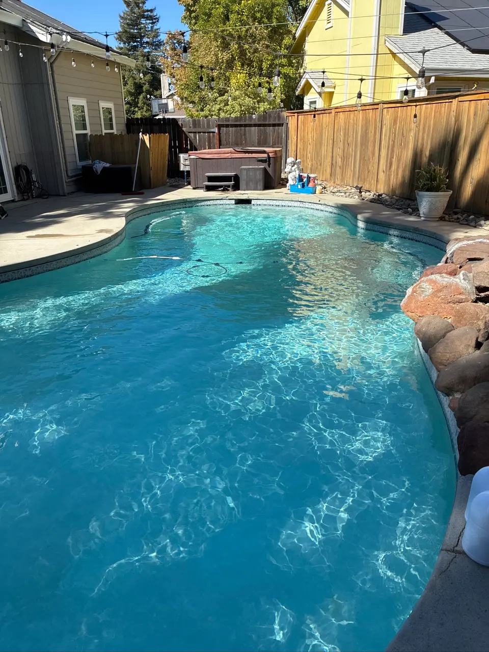Clear turquoise water fills a freeform pool with rock edging, waterline tile, and a separate covered hot tub, after pool service in Antelope, CA