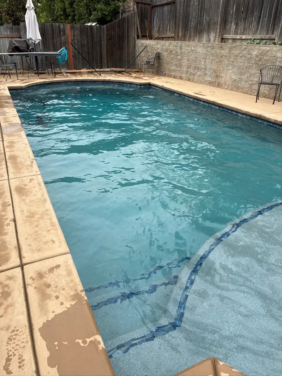Clear turquoise pool water with curved entry steps, blue tile edging, and tan stone coping, after pool service in Antelope, CA