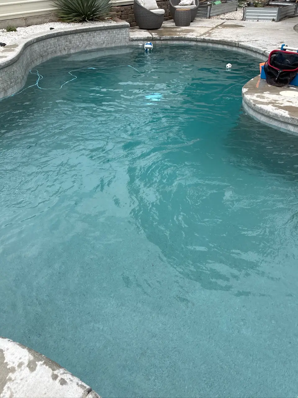Clear turquoise water fills a curved pool with gray tile, submerged steps, stone coping, and desert landscaping, after pool service in Antelope, CA