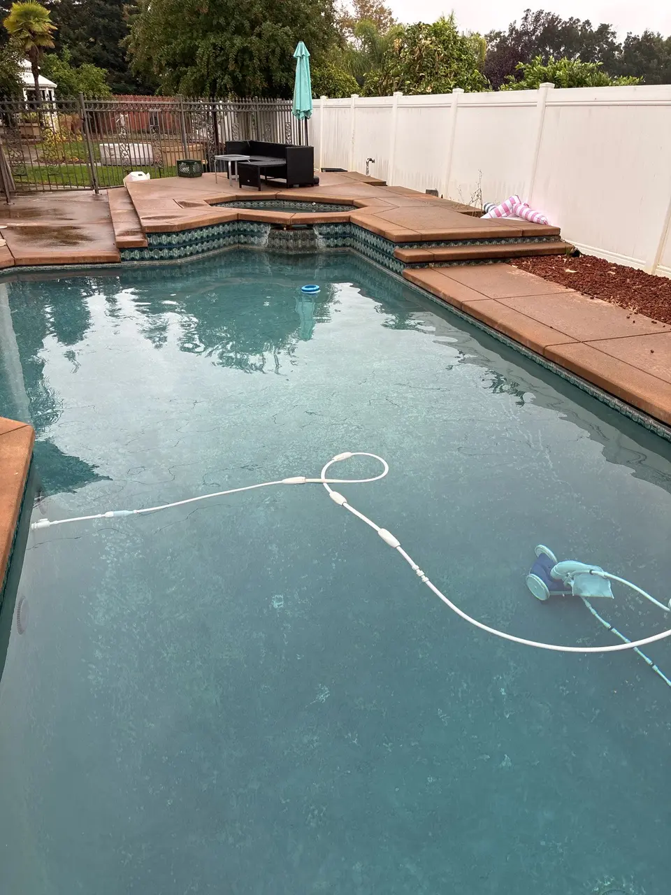Clear blue water fills a pool with decorative tile, a raised spillover spa, and a submerged cleaner, after pool service in Antelope, CA