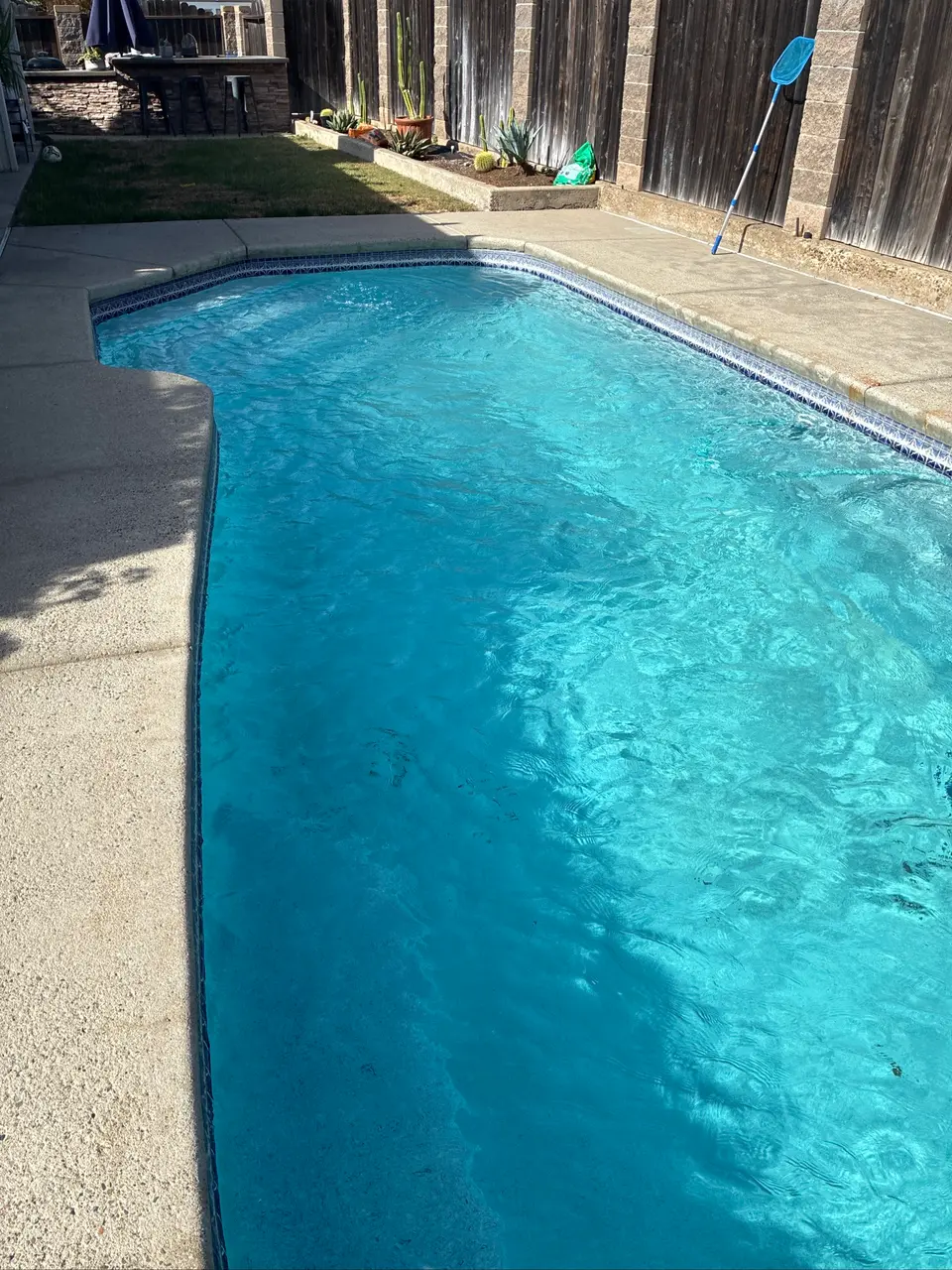 Clear turquoise pool water reveals entry steps, bordered by blue tile, concrete decking, and a raised planter, after pool service in Antelope, CA