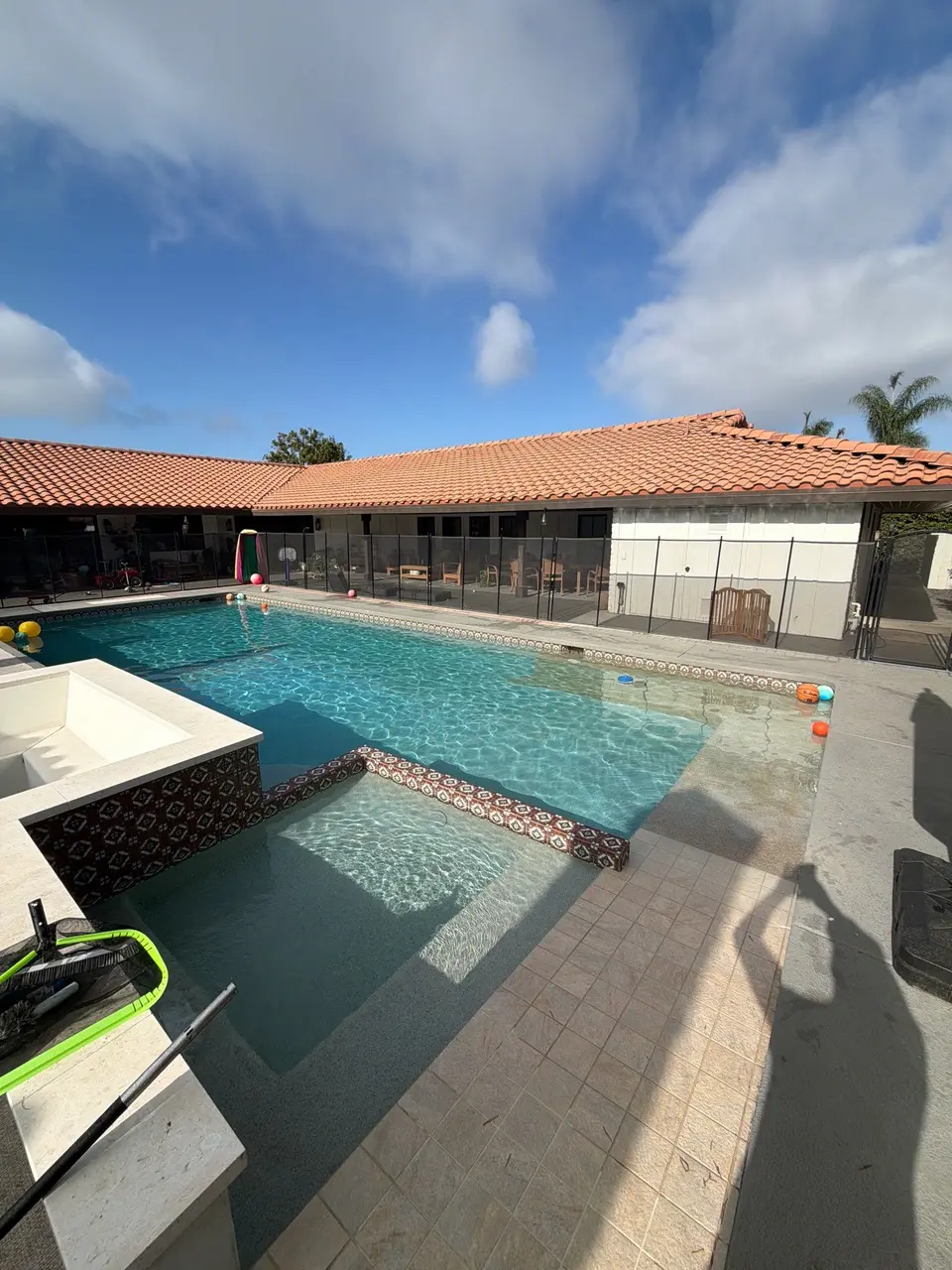 Pool and attached spa have sparkling blue water, decorative patterned tile, and wide submerged entry steps, after pool service in Carlsbad, CA