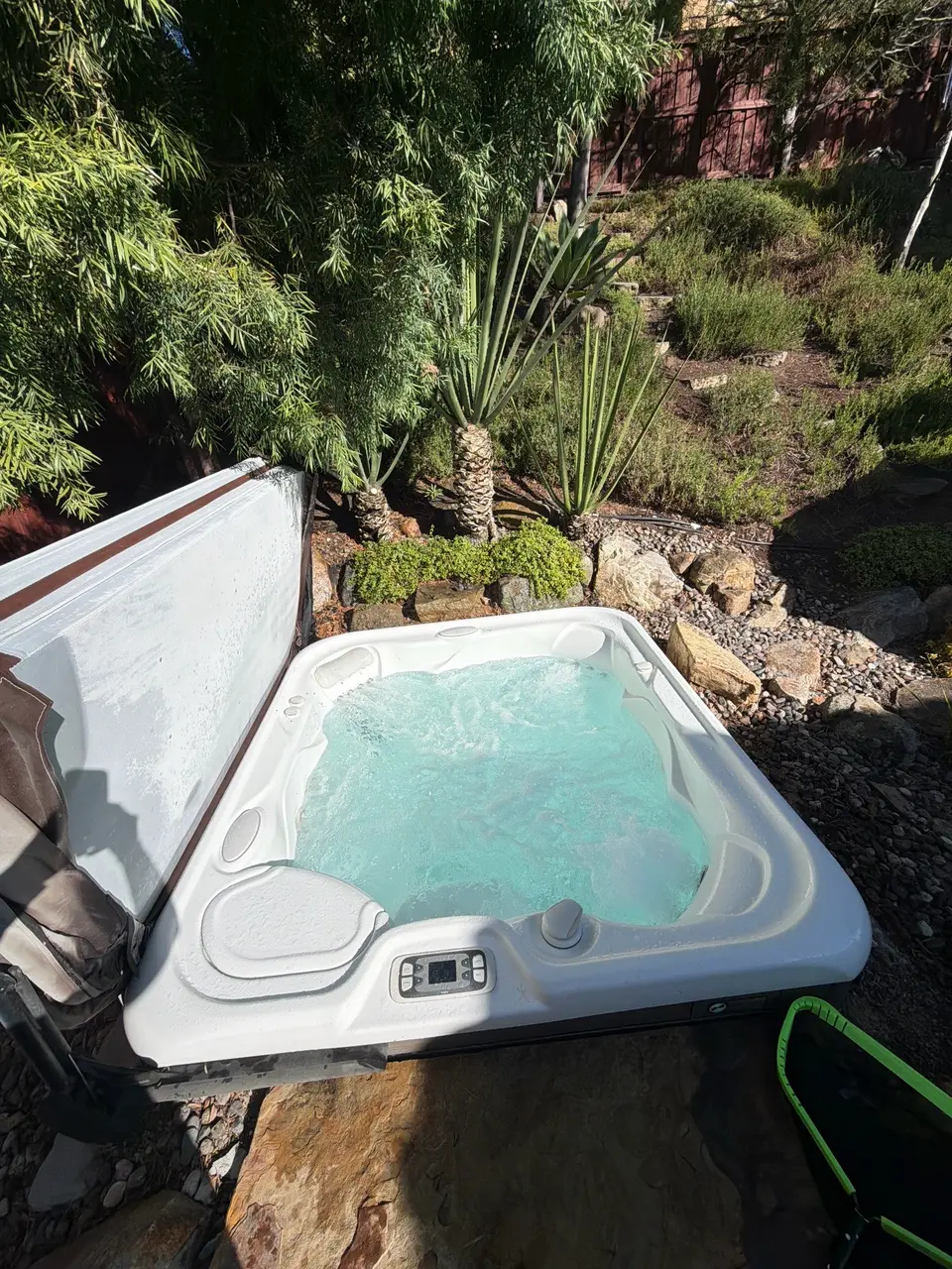 White spa with clear turquoise water and bubbling jets sits among rocks and dense greenery, after pool service in Carlsbad, CA