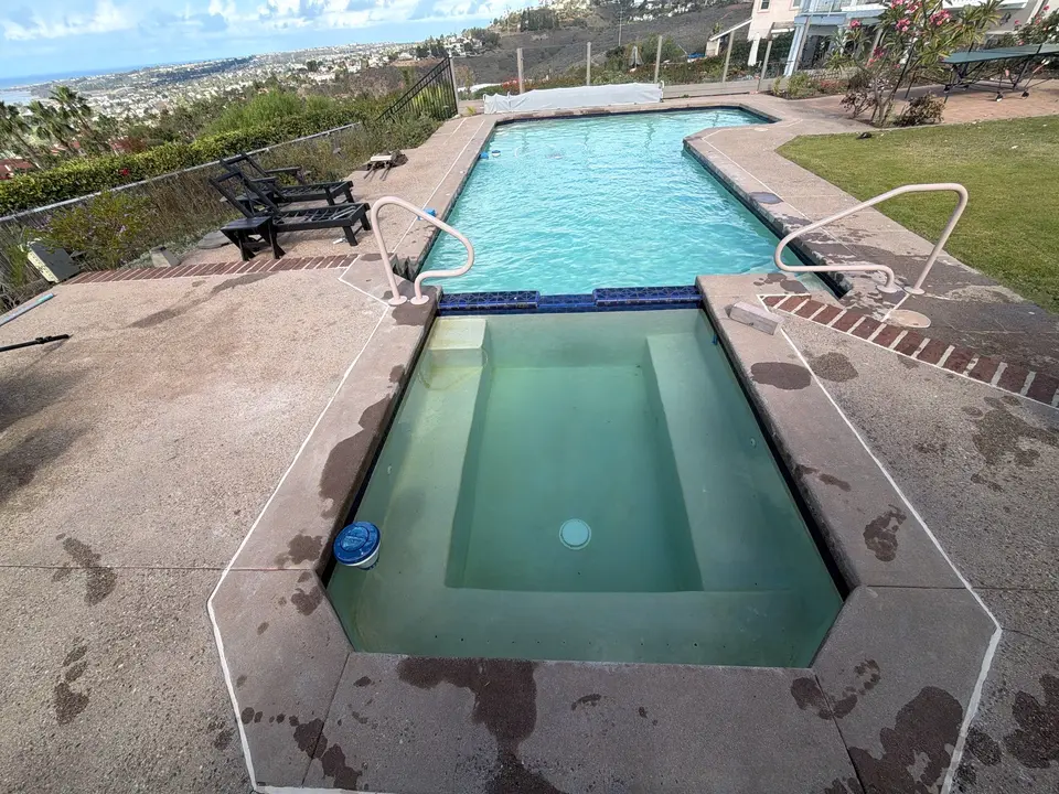 Clear blue pool with an attached spa, blue tile, entry handrails, and surrounding lawn and landscaping, after pool service in Carlsbad, CA
