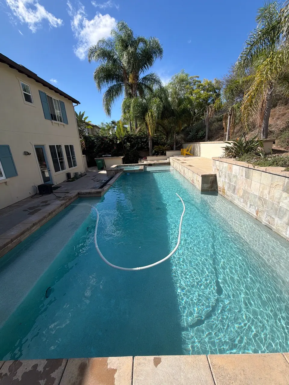 Sparkling turquoise pool with submerged steps, a raised spa, stone-tiled walls, and surrounding palms, after pool service in Carlsbad, CA
