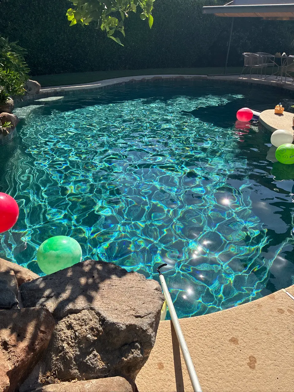 Sparkling turquoise water fills a freeform pool with rock edging, submerged steps, and colorful floating balls, after pool service in Carmichael, CA