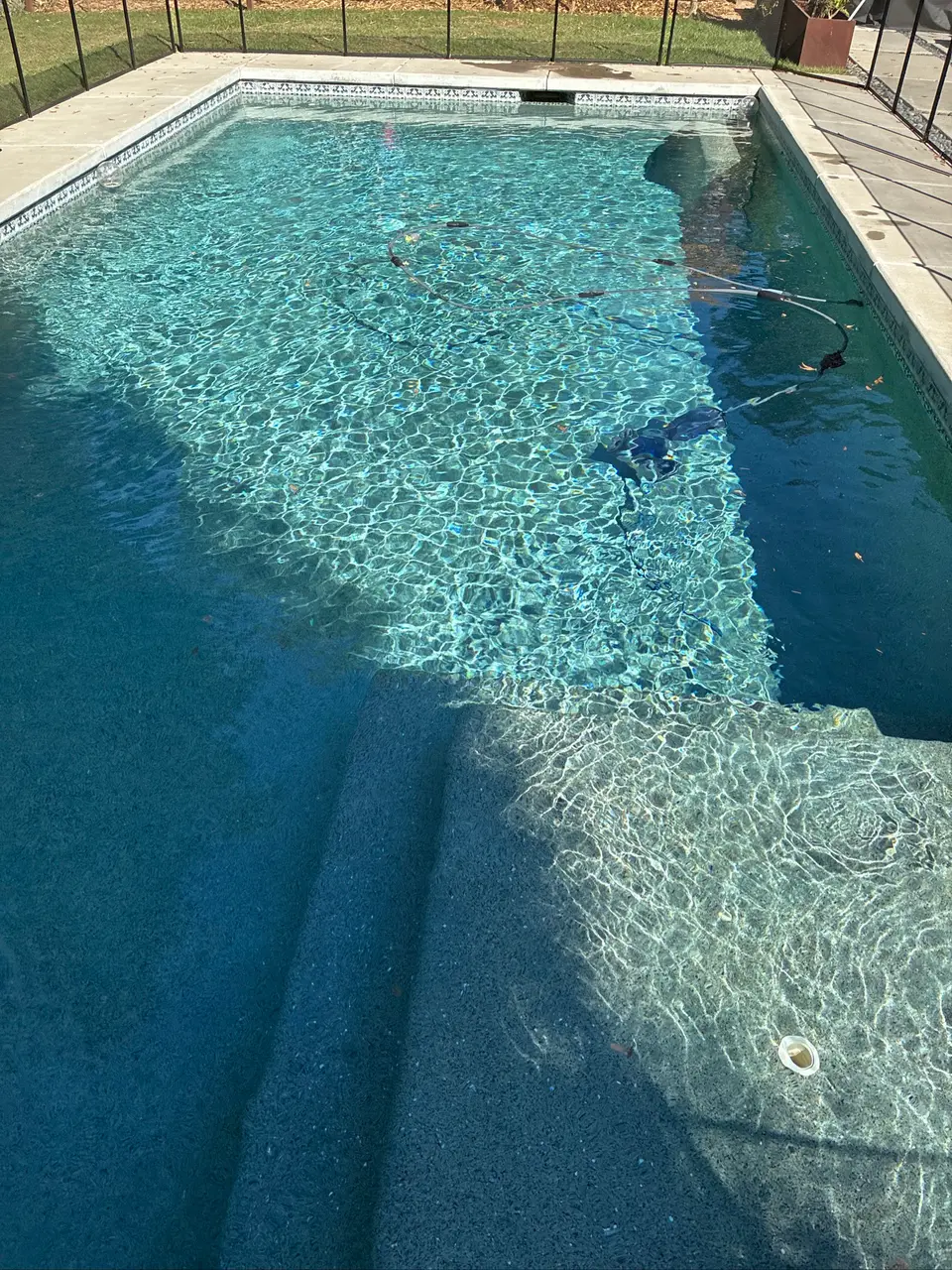 Clear blue water reveals broad entry steps and a speckled finish, with cleaning equipment beneath a screen enclosure, after pool service in Carmichael, CA