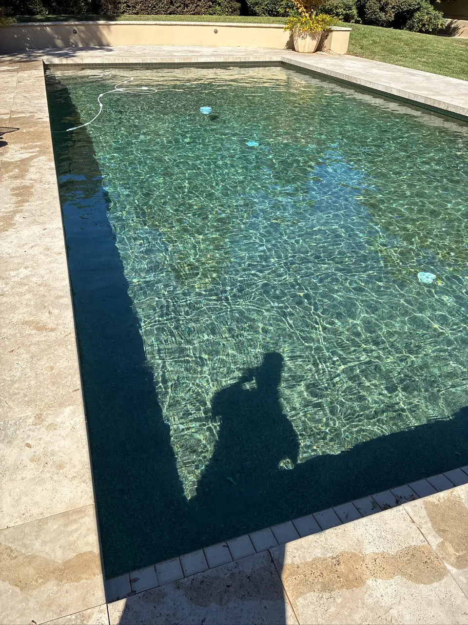Sparkling clear water reveals a dark rectangular pool with underwater steps, stone coping, and surrounding landscaping, after pool service in Carmichael, CA