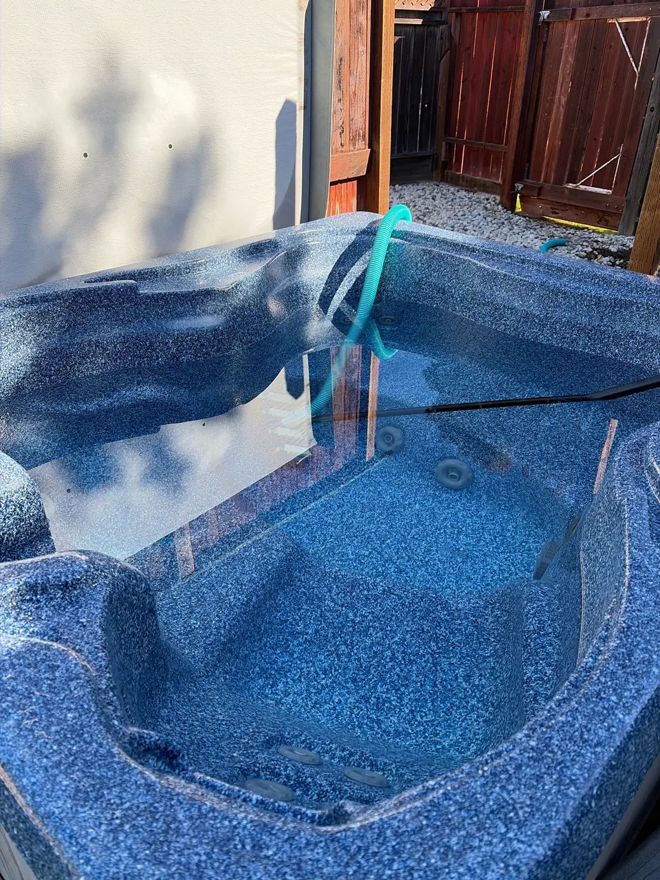 Spa with clear blue water, a speckled finish, molded seating, visible jets, and a cleaning hose, after spa drain in Carmichael, CA