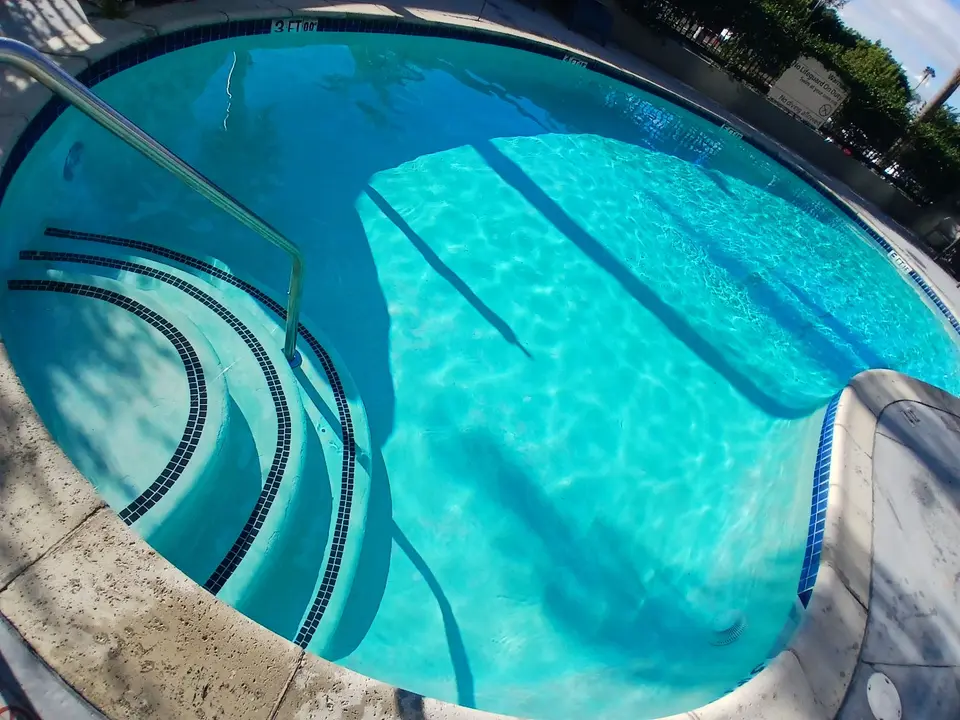 Sparkling turquoise water reveals curved entry steps with blue tile trim and a stainless steel handrail, after pool service in Carson, CA