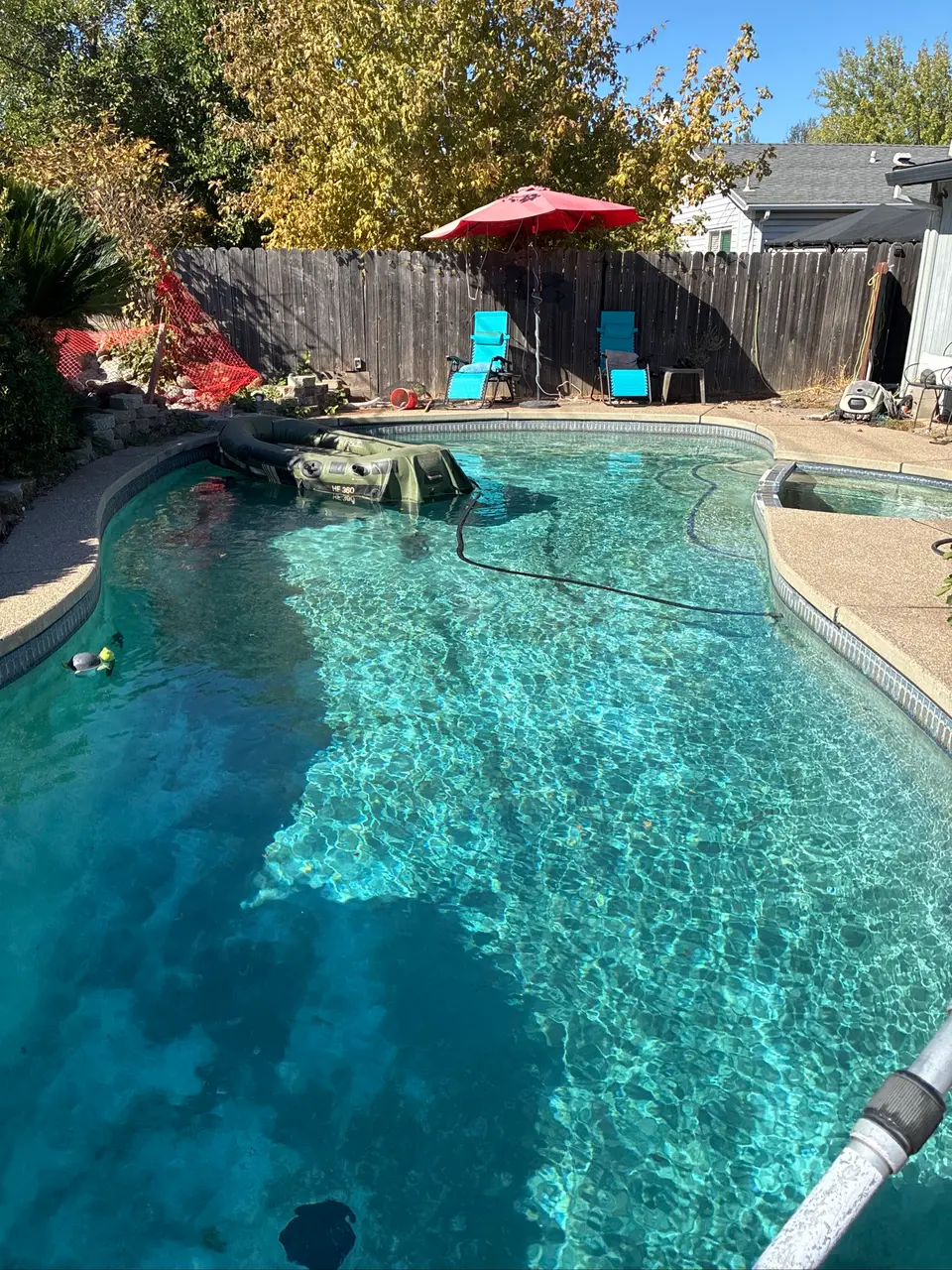 Sparkling turquoise pool with a pebble finish, attached spa, floating inflatable boat, and tree-lined patio, after pool service in Citrus Heights, CA
