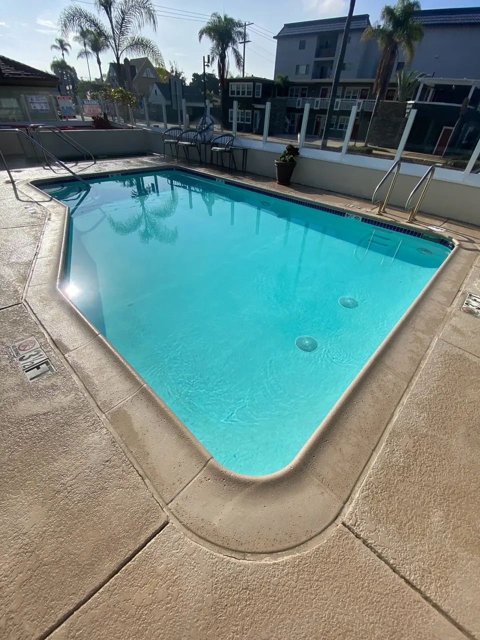 Sparkling turquoise pool with blue waterline tile, metal handrails, glass fencing, and surrounding palm trees, after callback in Coronado, CA