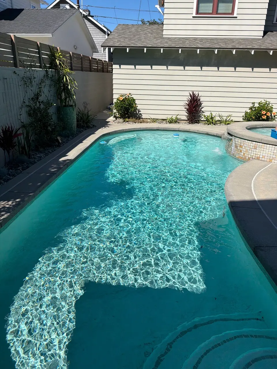 Sparkling turquoise pool with curved entry steps, a raised tiled spa, and landscaped borders, after pool service in Coronado, CA