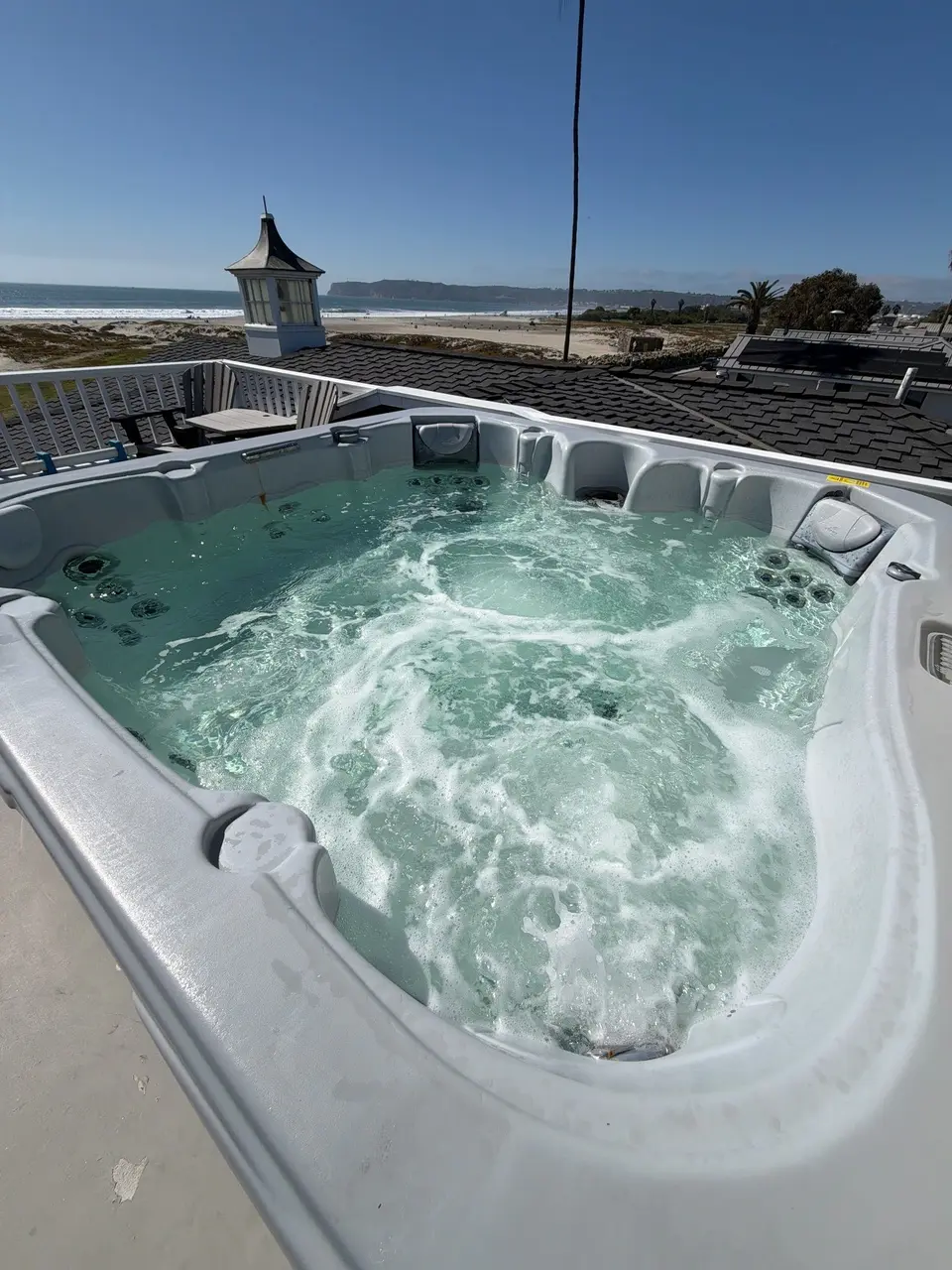 Clear turquoise water bubbles in a white spa with built-in seating and an ocean backdrop, after pool service in Coronado, CA
