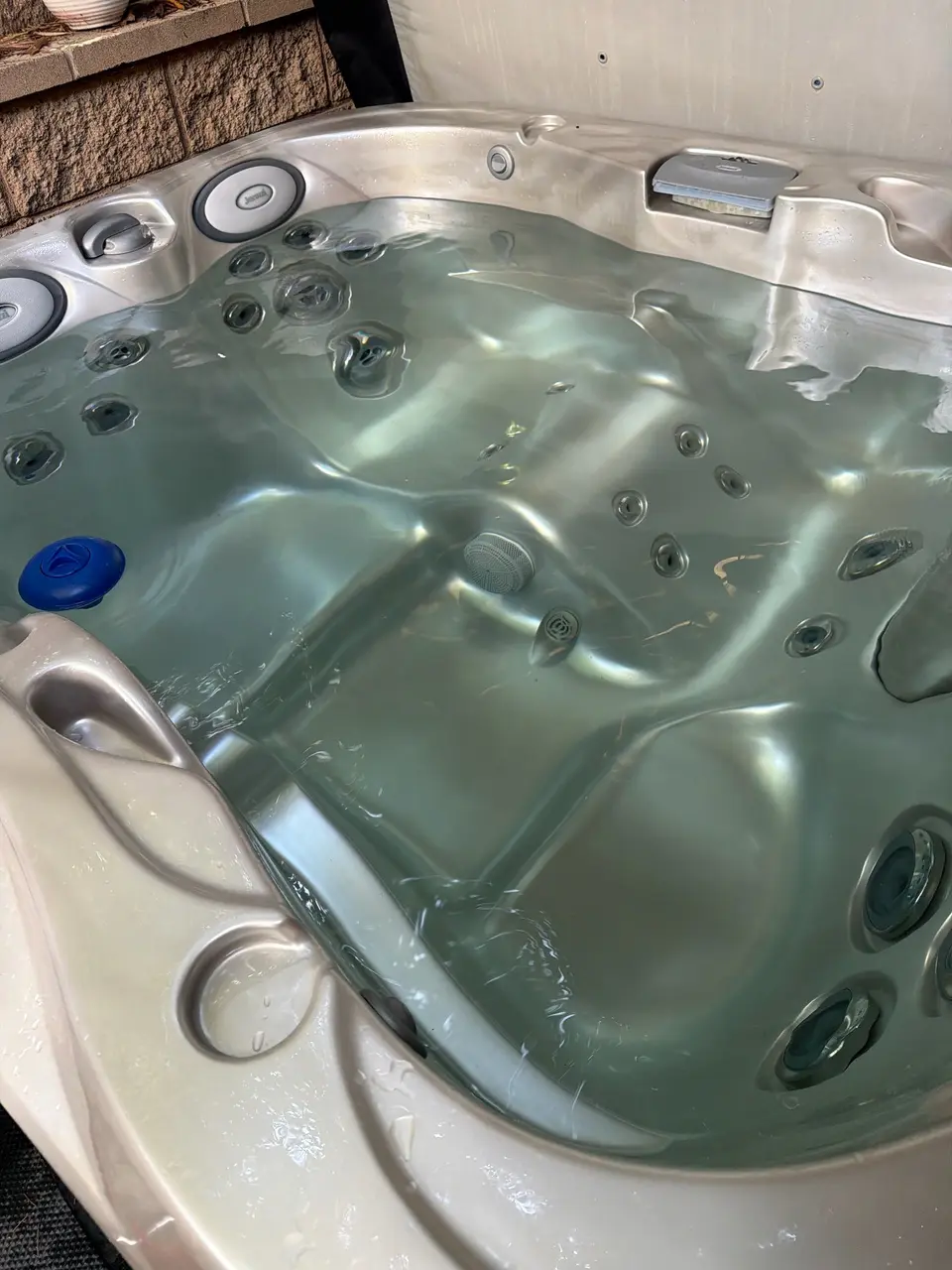 Clear water reveals molded seating and multiple jets in a beige spa with padded headrests, after pool service in Coronado, CA