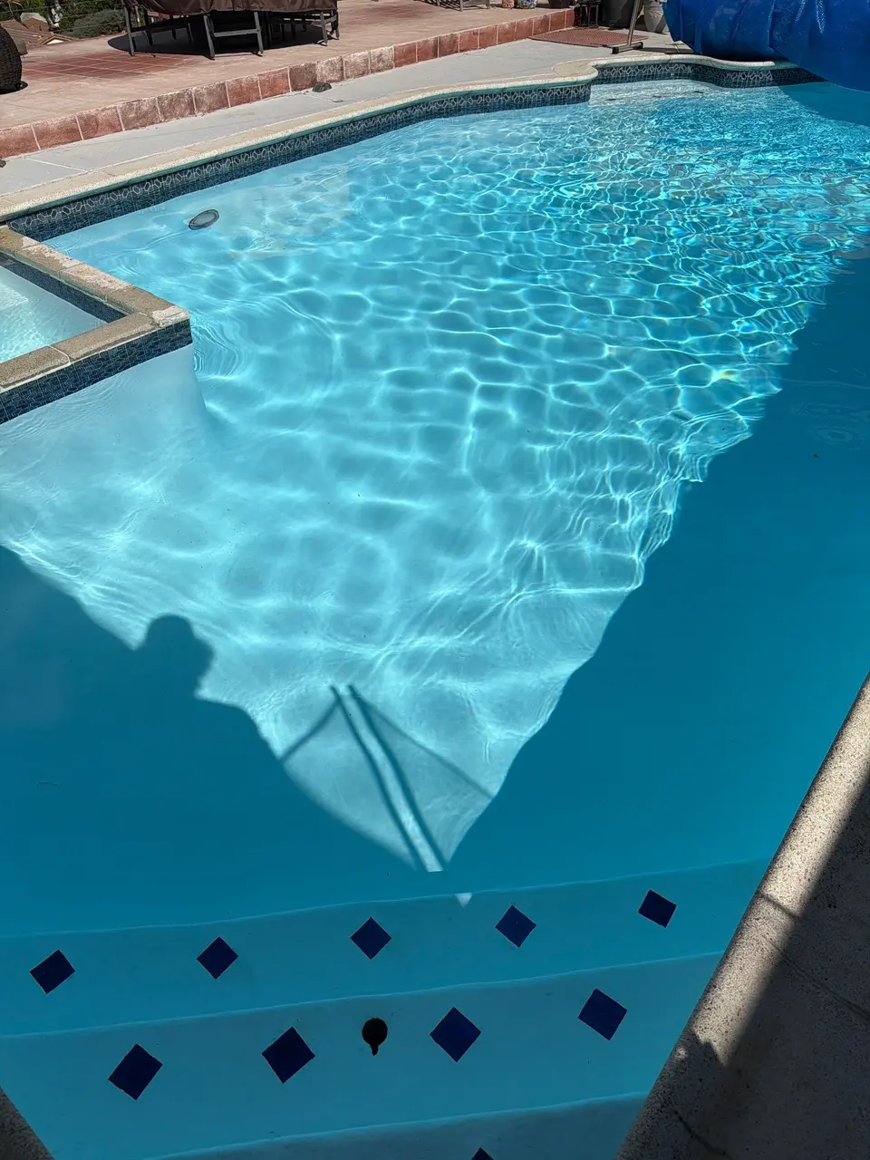 Sparkling blue pool water reveals diamond-accented entry steps beside an attached spa and decorative waterline tile, after pool service in Coronado, CA
