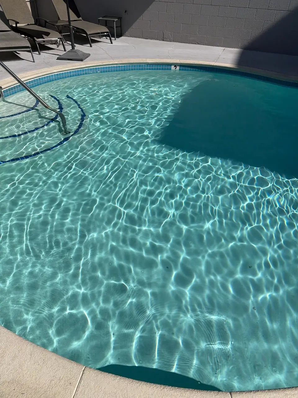Sparkling turquoise water reveals curved entry steps with blue tile accents and a stainless steel handrail, after pool service in Coronado, CA