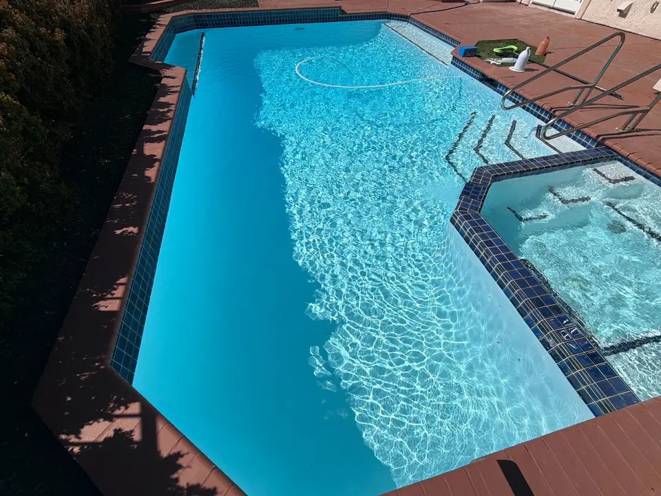 Sparkling blue pool with an attached spa, dark tile borders, entry steps, and metal handrails, after pool service in Del Mar, CA