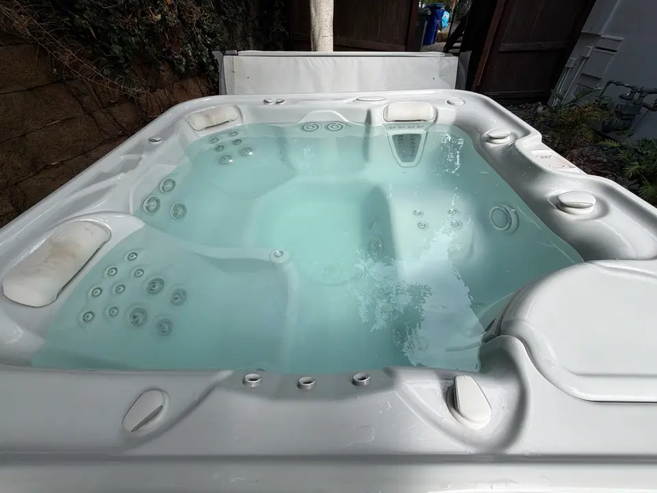 Clear pale turquoise water fills a white spa with molded seating, multiple jets, and discolored headrests, after pool service in Del Mar, CA