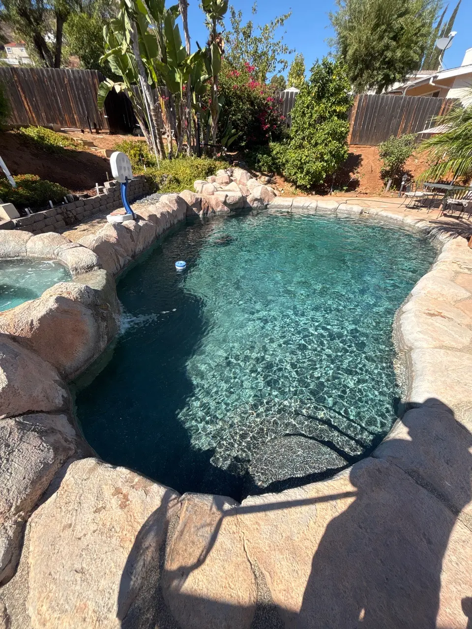 Sparkling turquoise water fills a rock-bordered pool with entry steps, a raised spa, and tropical landscaping, after pool service in El Cajon, CA