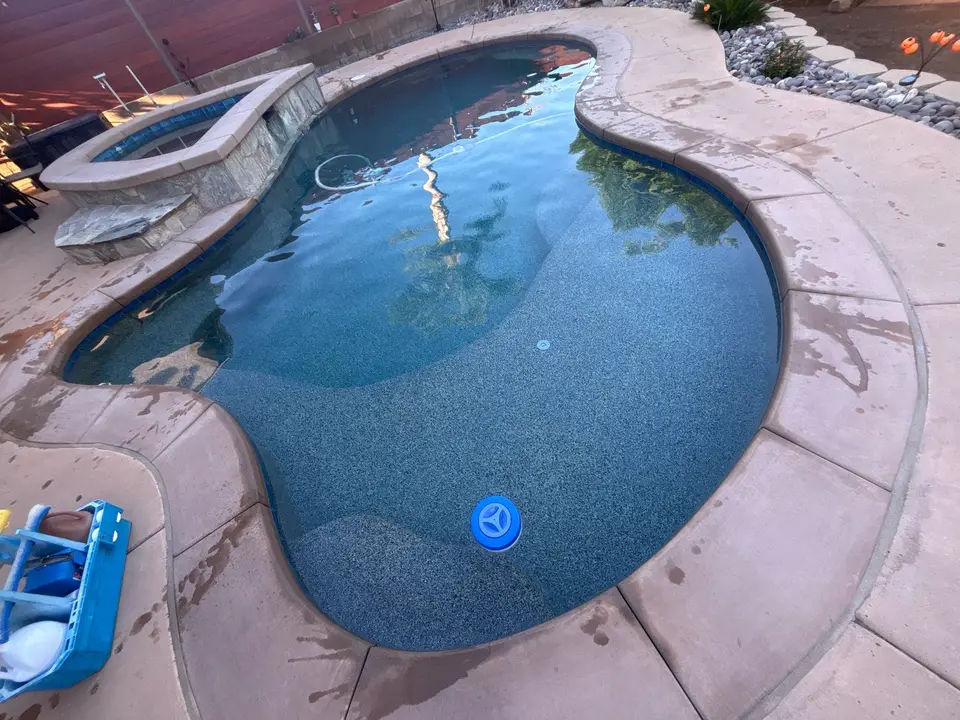 Clear blue water fills a freeform pebble-finish pool with wide steps and a raised stone-clad spa, after pool service in El Cajon, CA