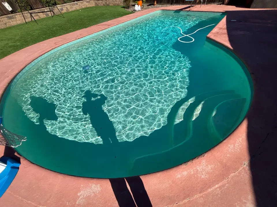 Sparkling turquoise pool water reveals curved entry steps, bordered by a pink deck and green lawn, after pool service in El Cajon, CA
