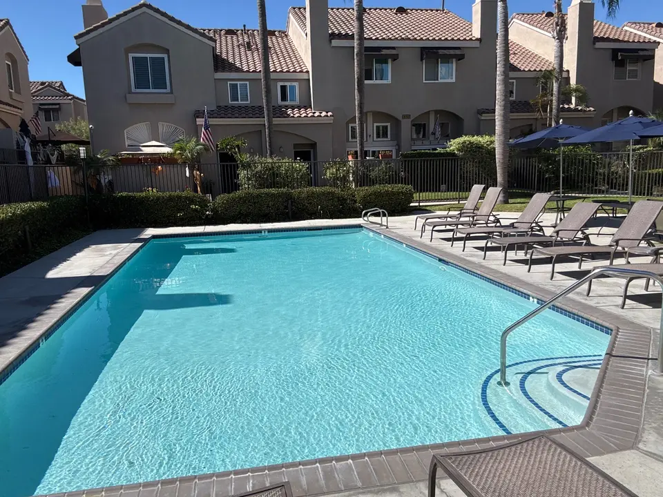 Sparkling turquoise pool with curved entry steps, blue tile, handrails, and surrounding lounge chairs and palms, after pool service in El Segundo, CA