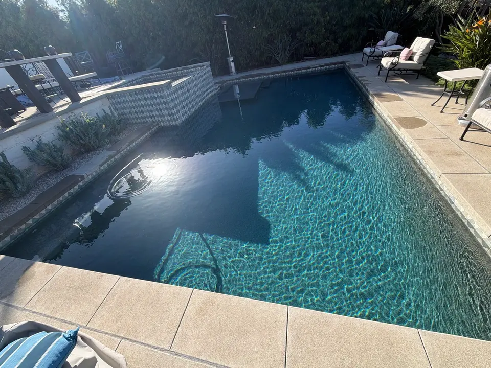 Sparkling blue pool water reveals submerged steps beside a raised tiled spa, stone decking, and landscaped borders, after pool service in Encinitas, CA