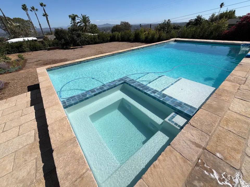 Sparkling turquoise pool and integrated spa feature blue tile trim, stone decking, and surrounding palms, after pool service in Encinitas, CA