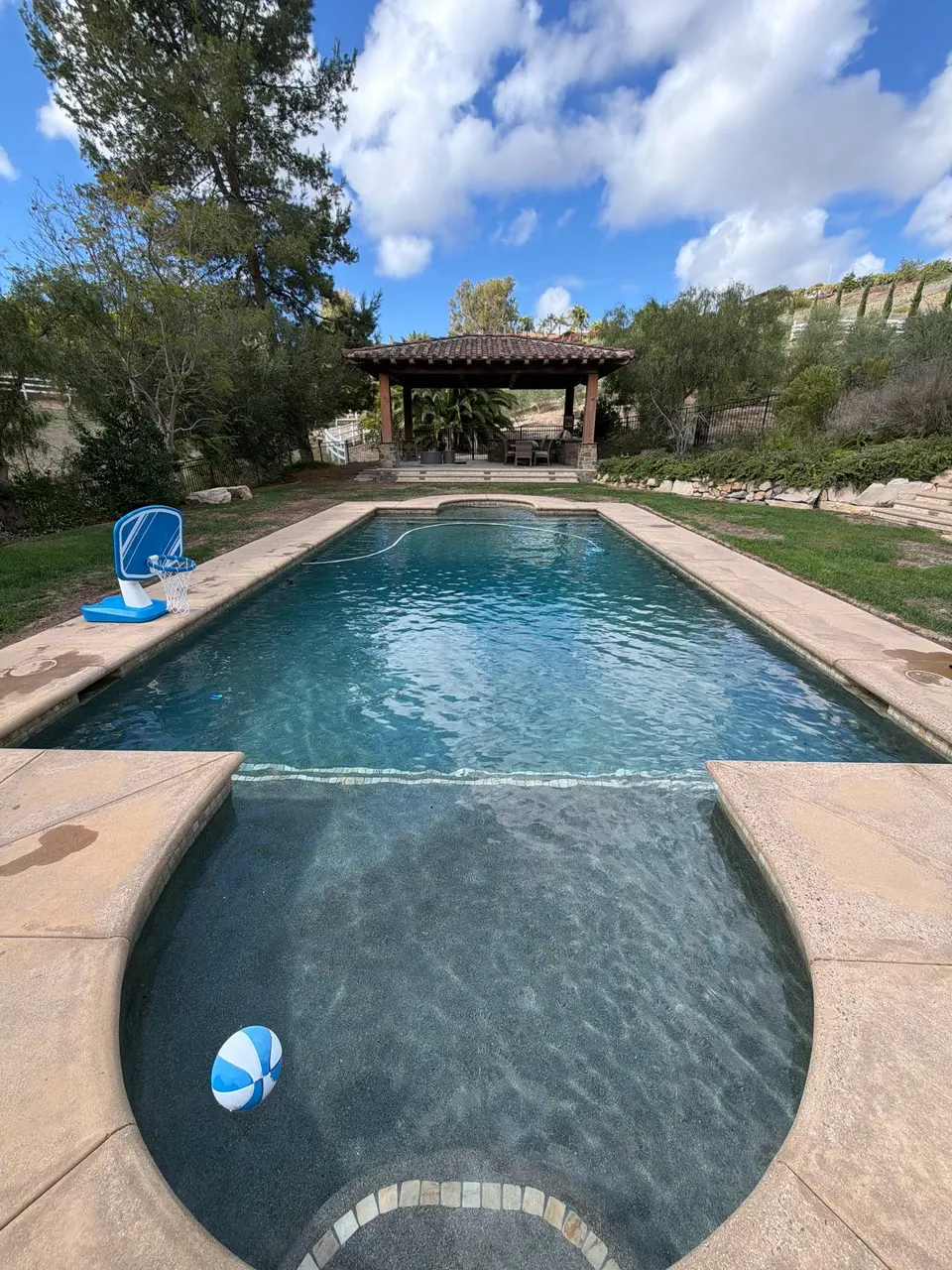 Clear teal water fills a dark-finished pool and attached rounded spa, surrounded by stone coping and landscaping, after pool service in Encinitas, CA