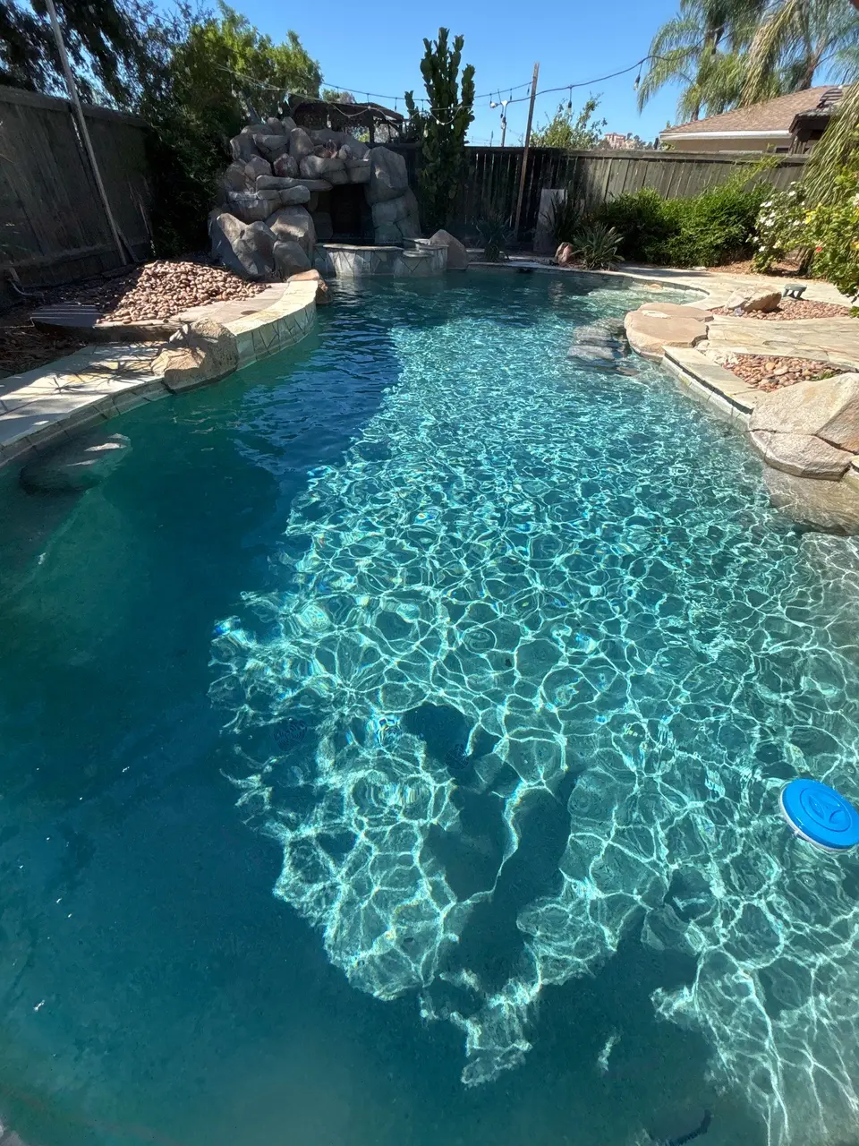 Sparkling turquoise water fills a freeform pool with stone coping, a rock grotto, and tropical landscaping, after pool service in Escondido, CA