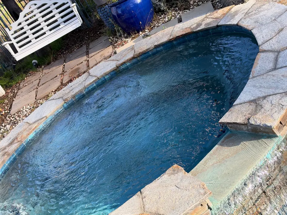Clear blue spa water is bordered by stone coping, blue tile, and a spillover waterfall, after pool service in Escondido, CA