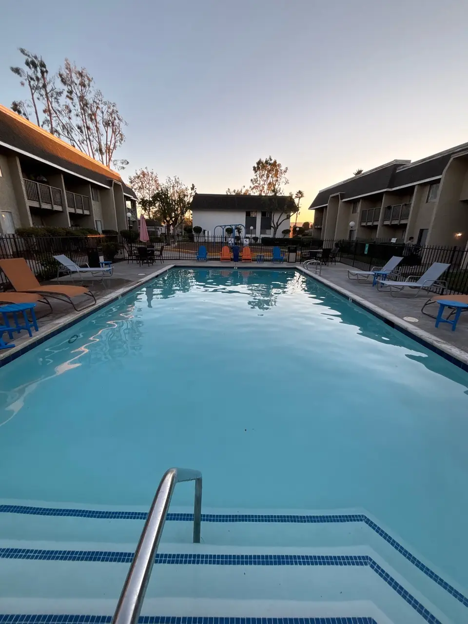 Clear blue water fills a rectangular pool with tile-trimmed steps, a metal handrail, and surrounding lounge chairs, after pool service in Escondido, CA