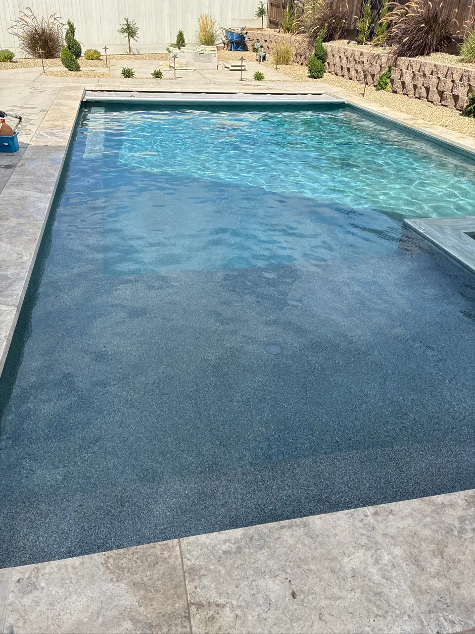 Clear blue water reveals a gray aggregate finish in a rectangular pool bordered by stone coping and landscaping, after pool service in Fair Oaks, CA