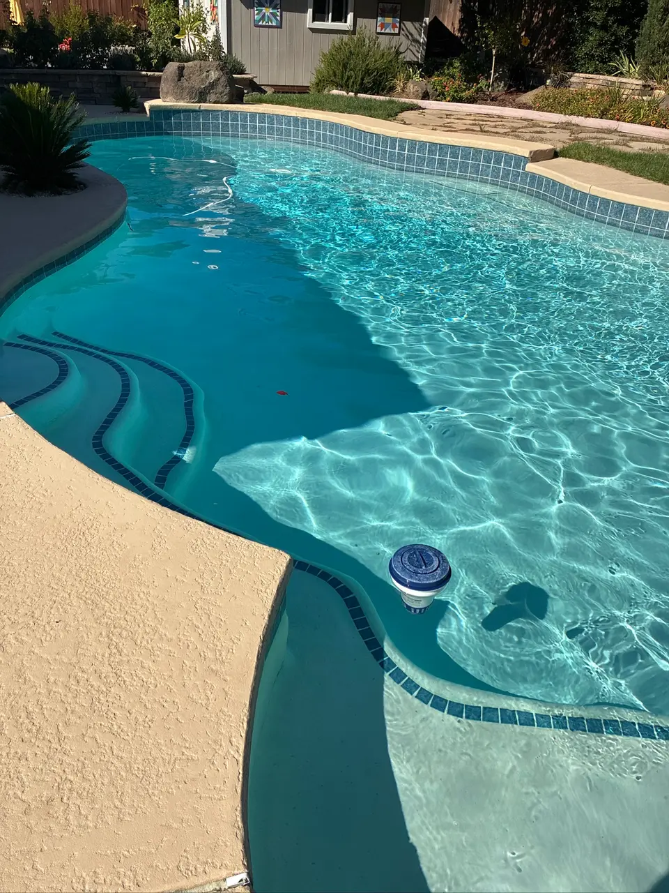 Sparkling turquoise water reveals curved tiled steps and a light finish, bordered by tan coping and landscaping, after pool service in Fair Oaks, CA