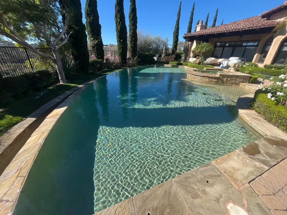 Sparkling turquoise pool with broad shallow steps, a raised stone spa, and mature landscaping, after callback in Fairbanks Ranch, CA