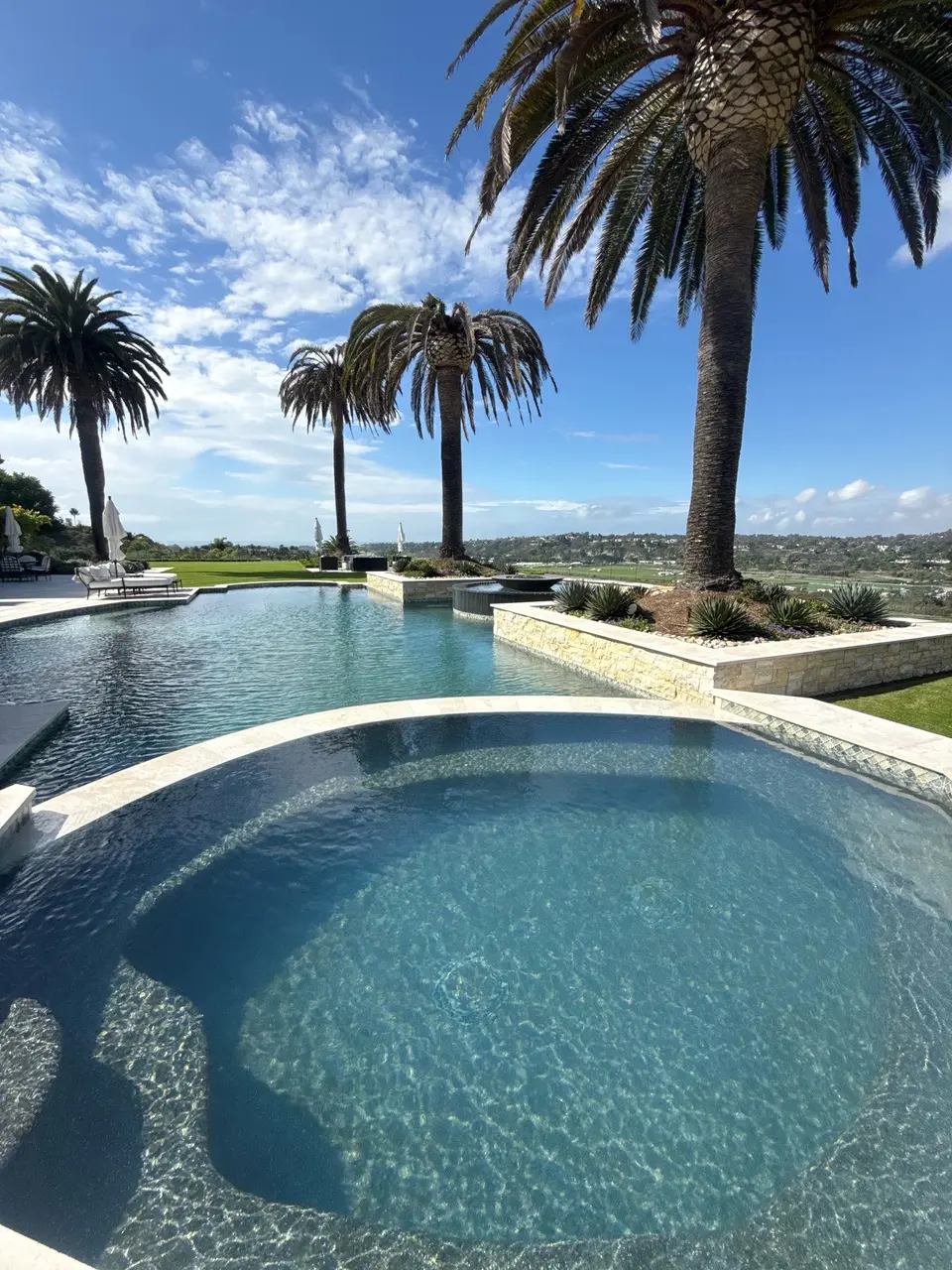 Sparkling blue pool and circular spa feature stone coping, submerged seating, and palm-lined landscaping, after phosphate treatment in Fairbanks Ranch, CA
