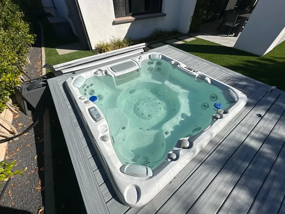 Clear pale turquoise spa water reveals molded seating and massage jets, surrounded by gray decking and landscaping, after pool service in Fairbanks Ranch, CA