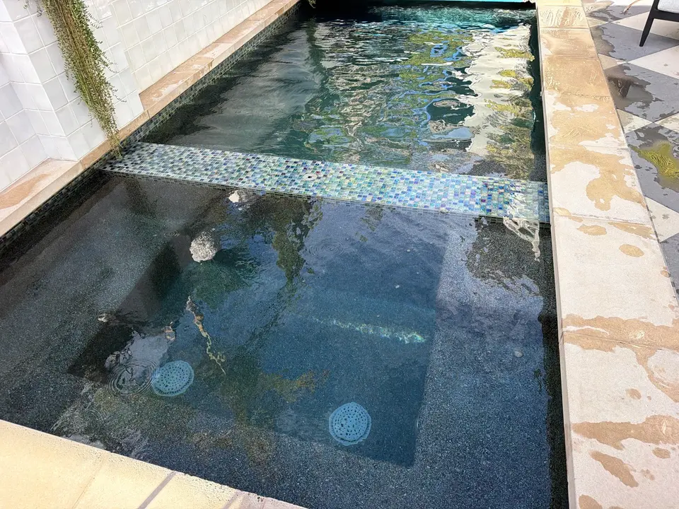 Clear dark teal water fills a narrow pool and spa separated by a mosaic-tiled divider, after pool service in Fairbanks Ranch, CA