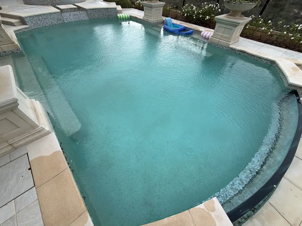 Clear turquoise water fills a curved pool with mosaic tile, submerged steps, stone coping, and decorative planters, after pool service in Fairbanks Ranch, CA