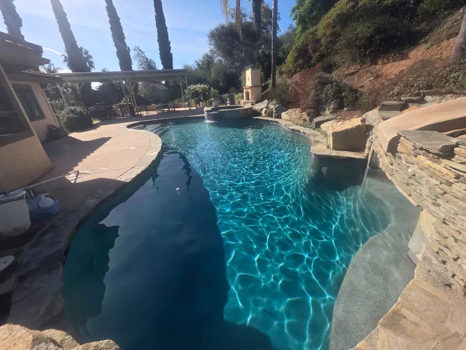 Sparkling blue water fills a curved pool with a raised spa, rock waterfall, and palm landscaping, after pool service in Fallbrook, CA