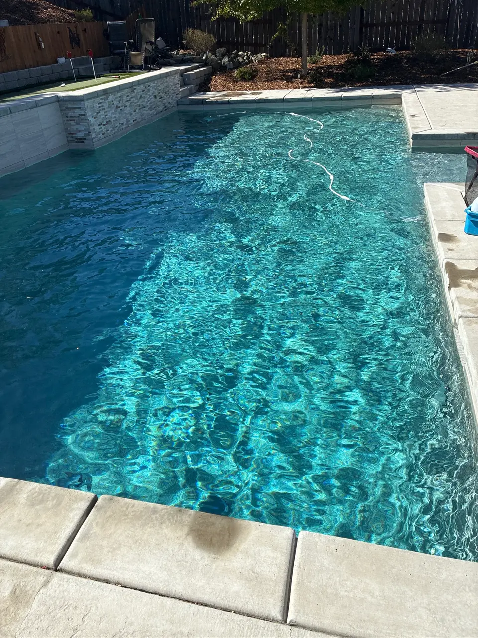 Sparkling turquoise pool water with underwater steps, light stone coping, and a raised tile accent wall, after pool service in Folsom, CA