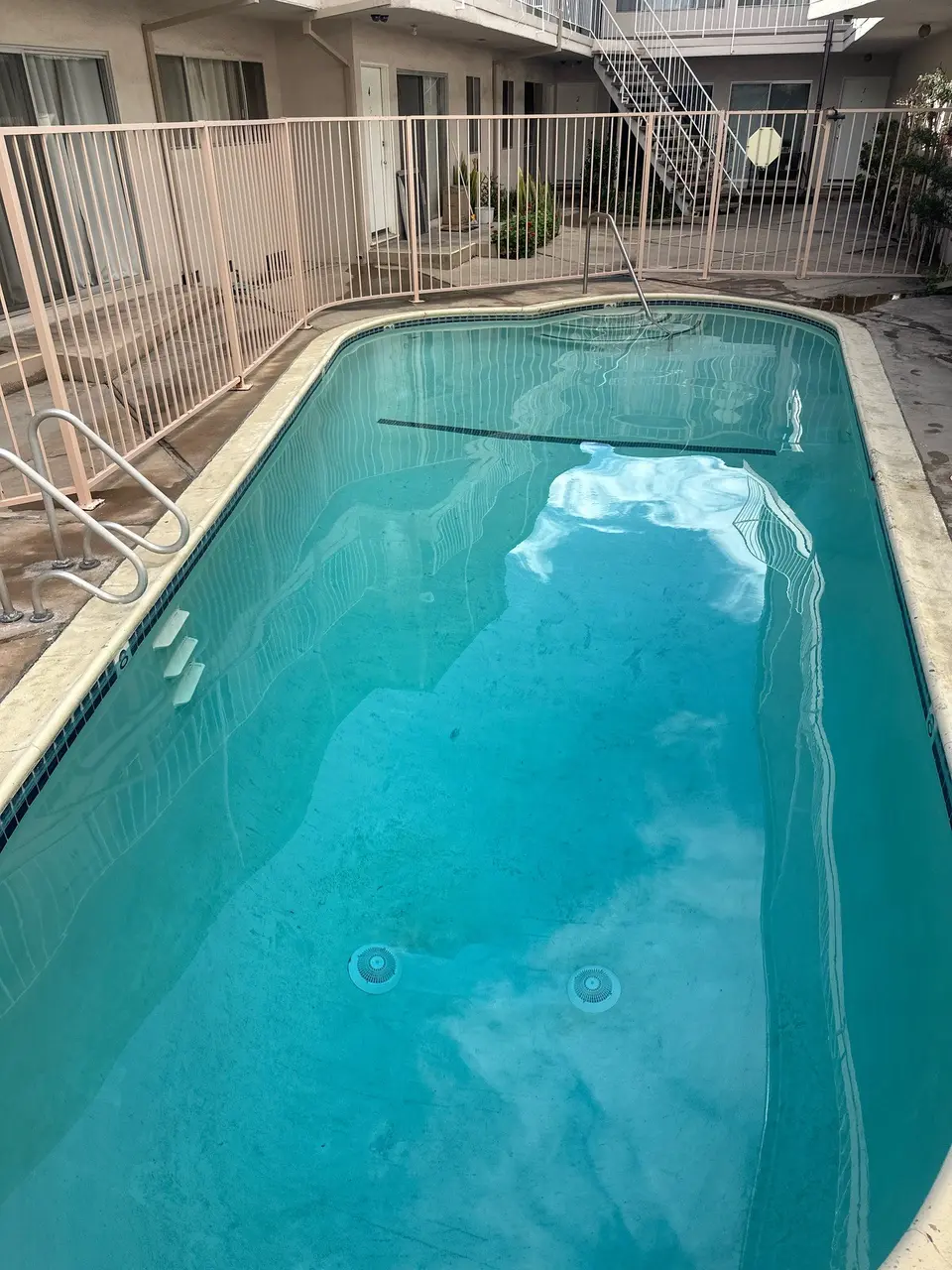 Clear turquoise water fills a fenced pool with metal handrails, entry steps, and visible floor discoloration, after pool service in Gardena, CA