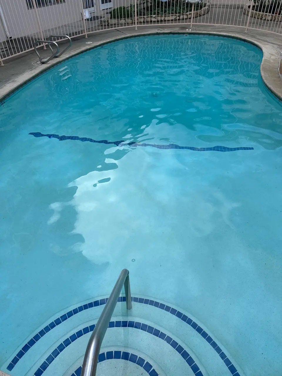 Clear turquoise pool water reveals blue tile accents and curved entry steps with a stainless steel handrail, after pool service in Gardena, CA