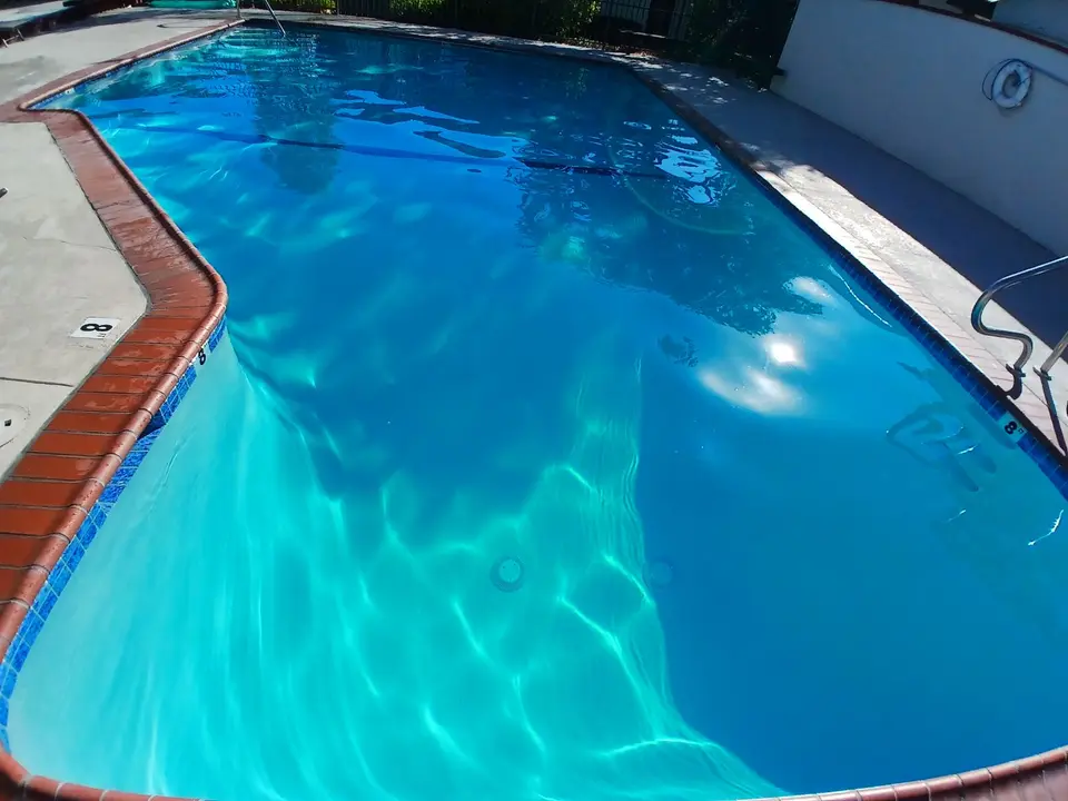 Sparkling blue pool water reveals the floor, bordered by blue tile, brick coping, and stainless steel ladders, after pool service in Harbor City, CA