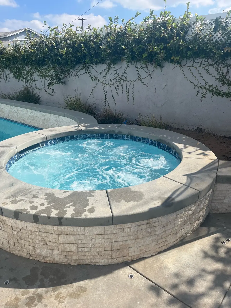 Clear blue water bubbles in a raised circular stone-clad spa beside a partially visible pool, after callback in Hawthorne, CA